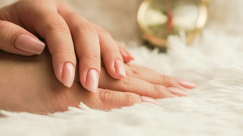 Mão com unhas nude em formato amêndoa sobre manta clara