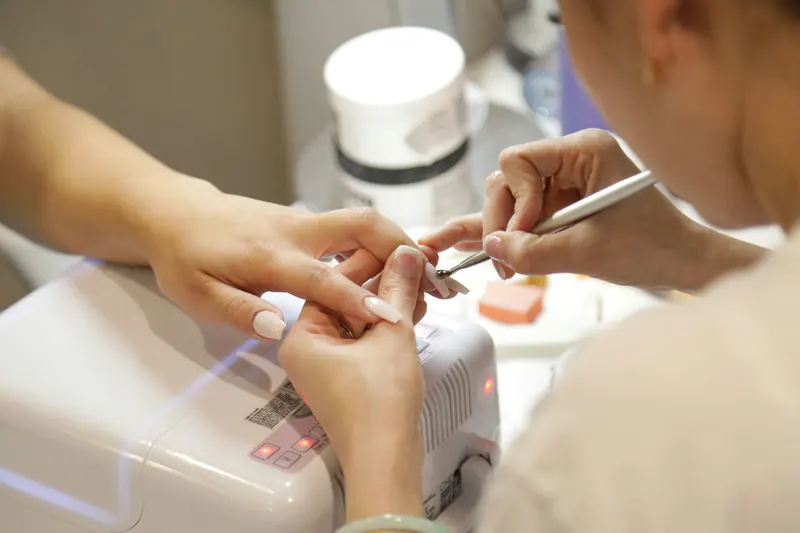 Nail designer fazendo a manutenção das unhas de uma cliente com cabine de LED